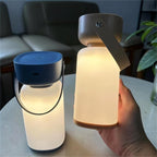 Clérachic cordless cylinder lamps glowing warm on a marble table, one with a blue top and one held in a hand.