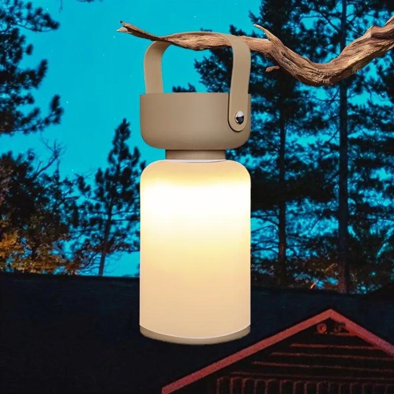 Clérachic cordless cylinder lamp with a taupe handle hung from a pine branch at dusk, glowing warm white before a cabin.