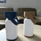 Clérachic cordless cylinder lamps side by side on a marble table, one with a blue handle and one with a brown handle.