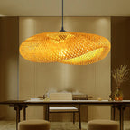 The Clérachic bamboo pendant lit above a dark timber dining table against a linen wall.