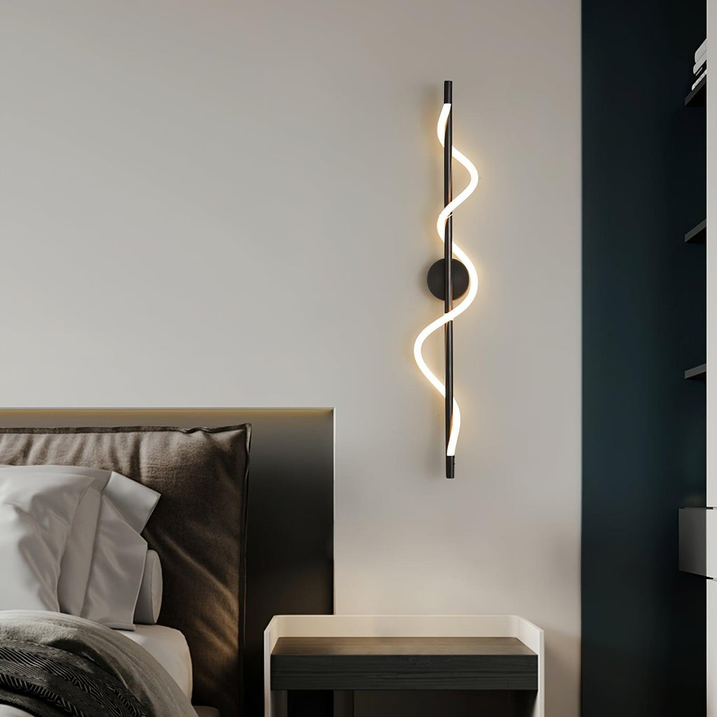 This Clérachic wall light in black has a lit silicone band twisting around a slim rod, beside a bed and a dark blue panel.