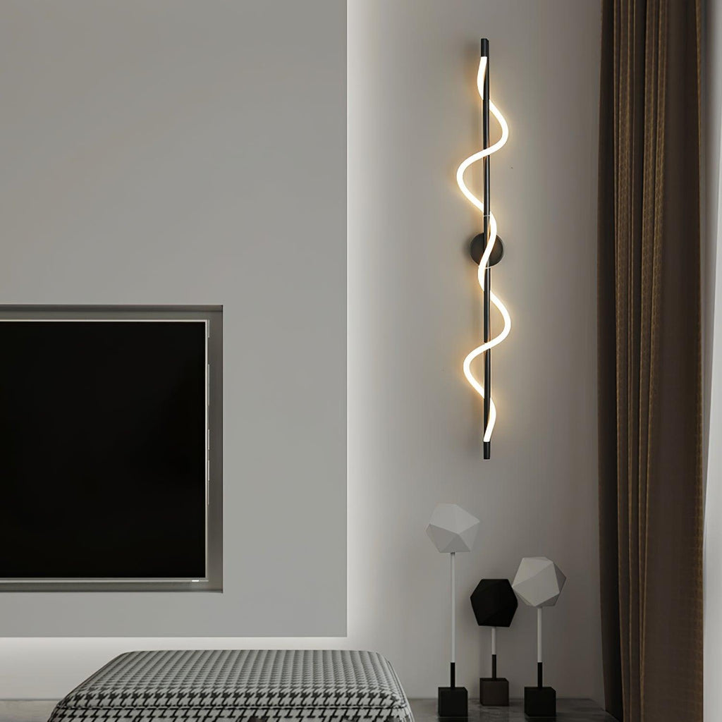 A tall black Clérachic wall light with a twisting lit band hangs by a wall-mounted screen above a houndstooth bed throw.