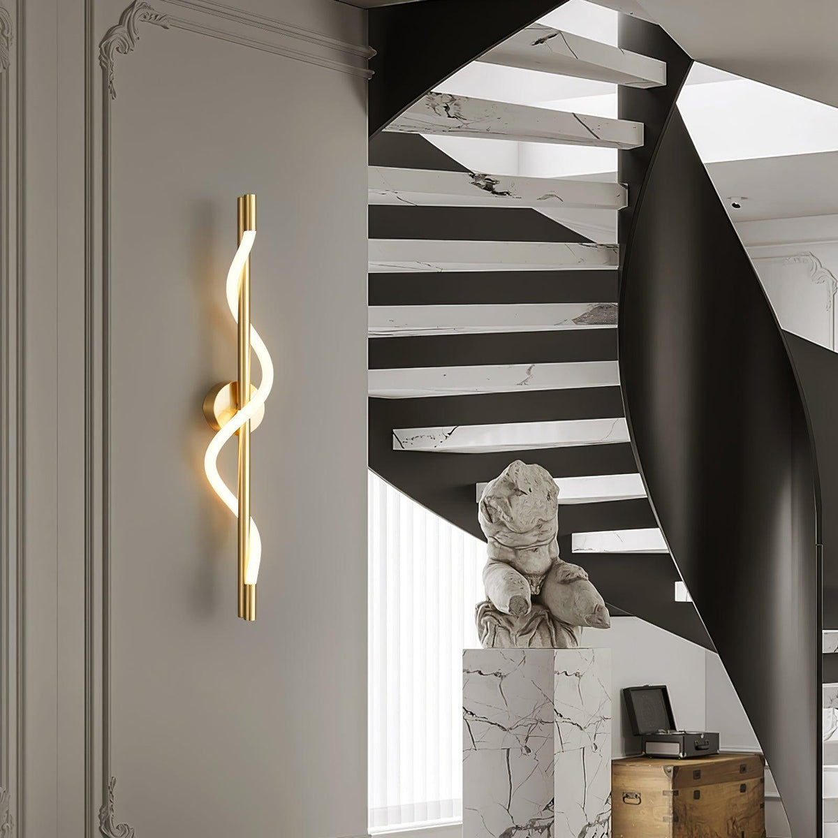 A brass Clérachic wall light with a lit spiral band glows on a pale wall beside a black curving staircase and a marble plinth.