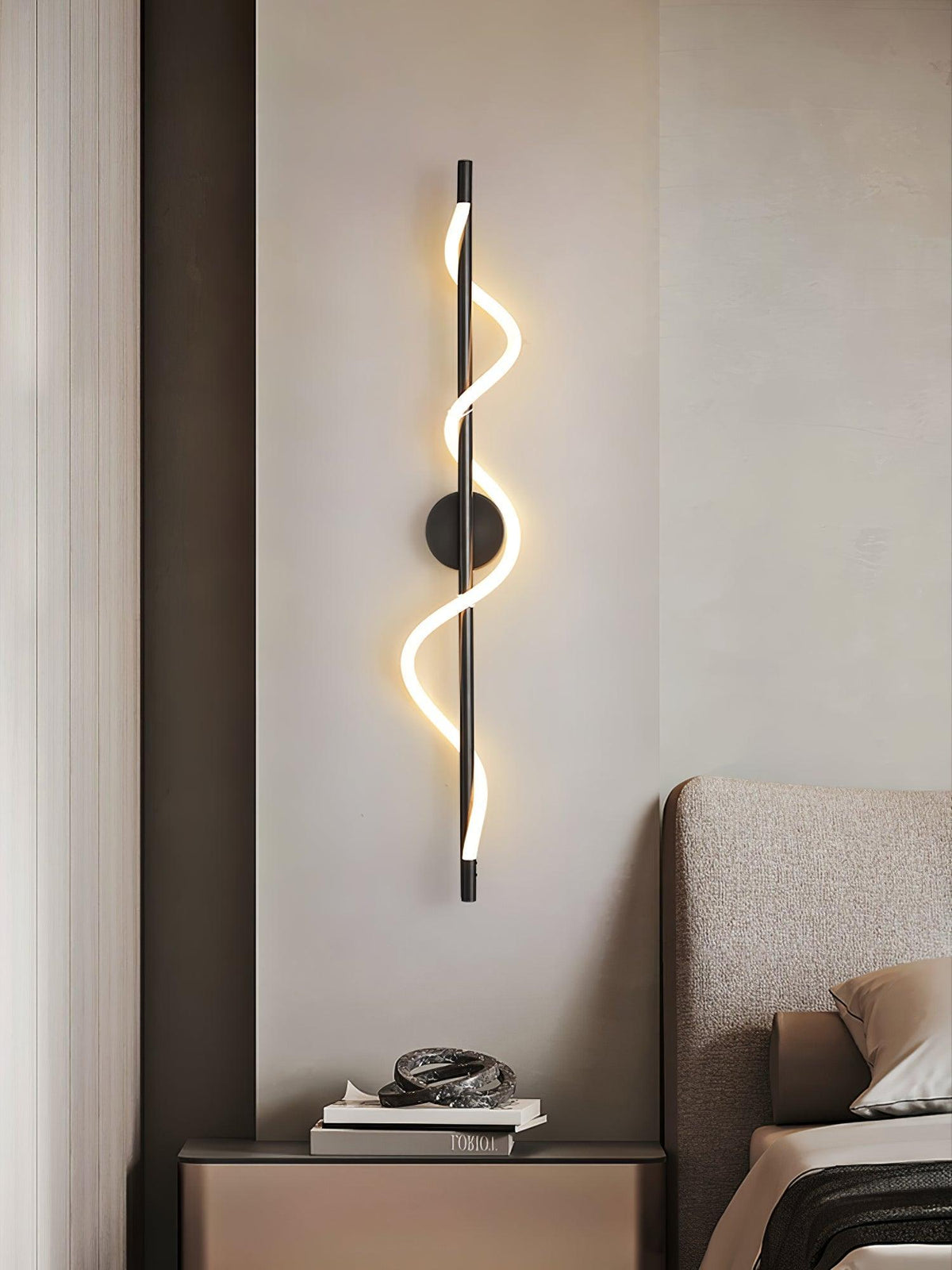 Above a bedside table in a beige bedroom, a black Clérachic wall light glows with a lit spiral band by a padded headboard.