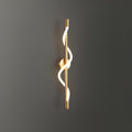 On a dark grey wall, a brass Clérachic wall light shows its glowing silicone spiral.