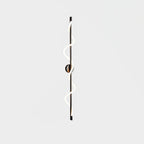 A long black Clérachic wall light with a two-turn lit spiral band and a round backplate, on a pale backdrop.