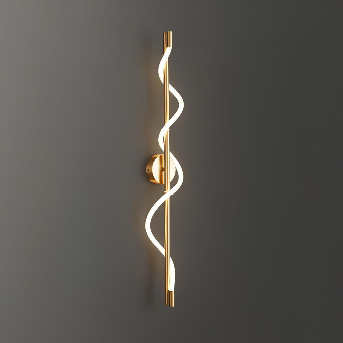 This brass Clérachic wall light has a lit two-turn spiral band and a round backplate, on a dark grey wall.