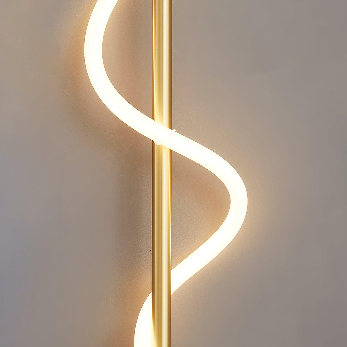 Close view of the glowing white silicone band curling around the brass rod of this Clérachic wall light.