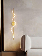 On a textured wall beside a sofa and a dark column, a brass Clérachic wall light glows with its lit spiral band.