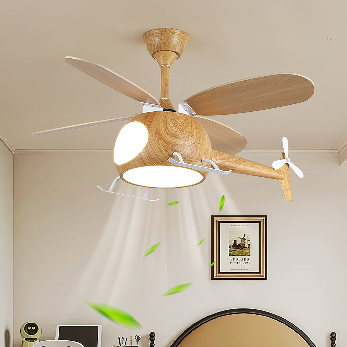 Close view of the helicopter fan from Clérachic with its light on, with leaves drifting in the airflow above a framed picture and a bedhead.