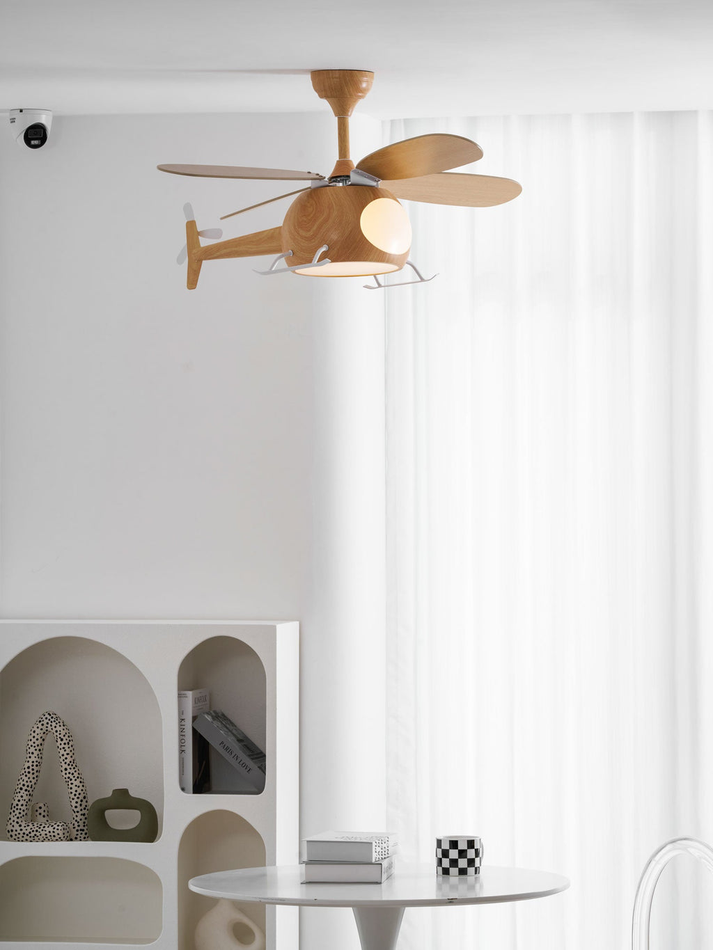 Side view of the helicopter fan from Clérachic against sheer white curtains, with an arched white shelf and a small round table below.