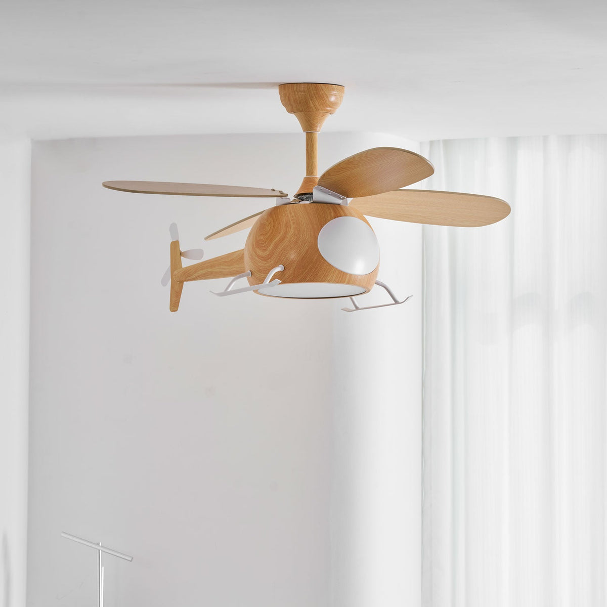Against a white wall, this Clérachic helicopter fan shows its four wood-grain blades and white skids in front of sheer curtains.