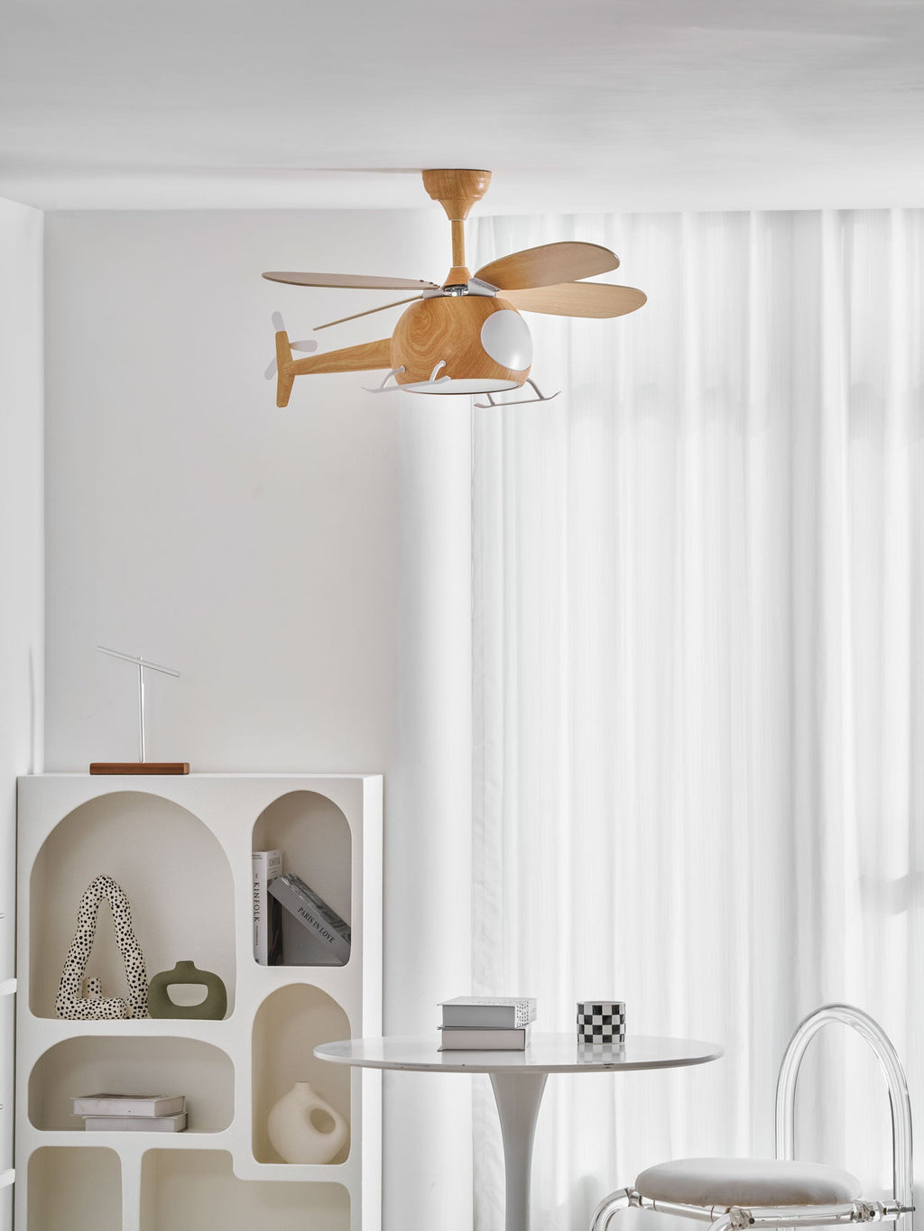 A small helicopter ceiling fan from Clérachic at the top of a white room, above an arched shelf unit and a round table with a chair.