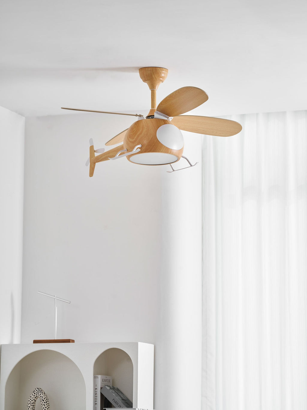 Helicopter ceiling fan from Clérachic seen from slightly below against sheer curtains, with the edge of an arched white shelf at the bottom.