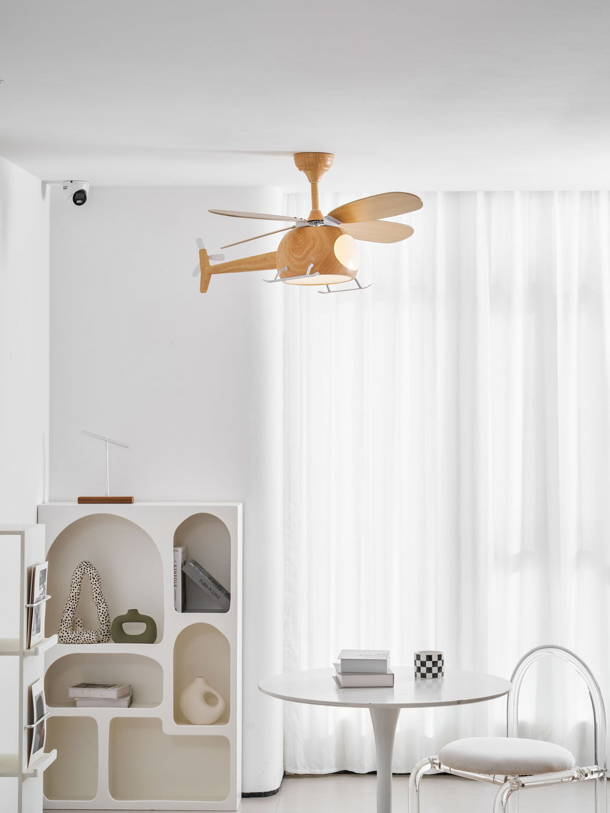 High on a white ceiling, a wood-grain Clérachic helicopter fan sits above an arched shelf unit and a round table far below.