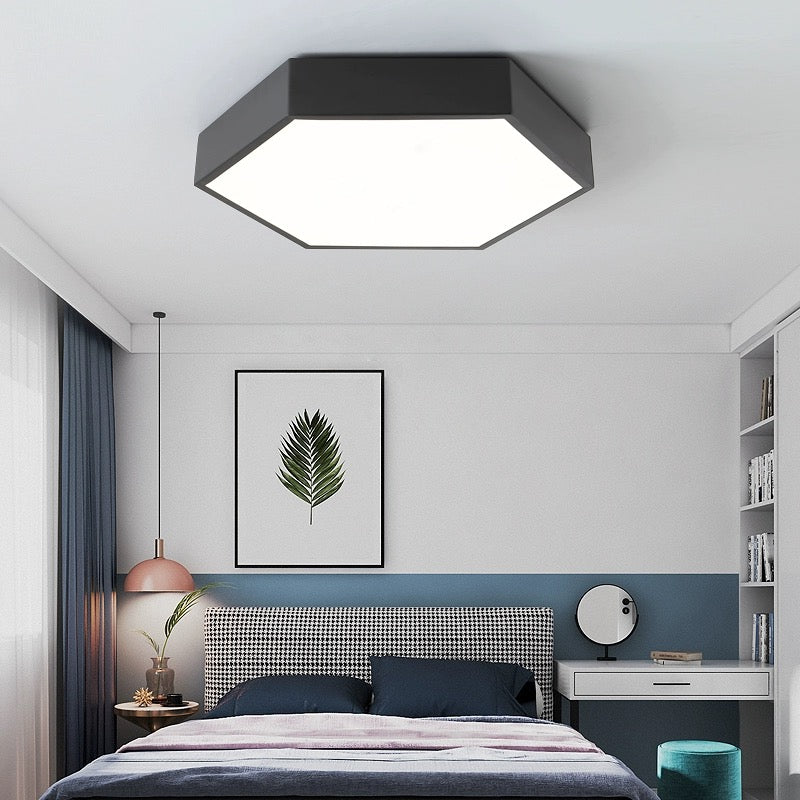 Black Clérachic hexagon LED flush mount ceiling light glowing above a bed with a leaf print and pendant lamp.