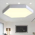 Warm-lit white Clérachic hexagon ceiling light in a living room with a wall-mounted TV and floor lamp.