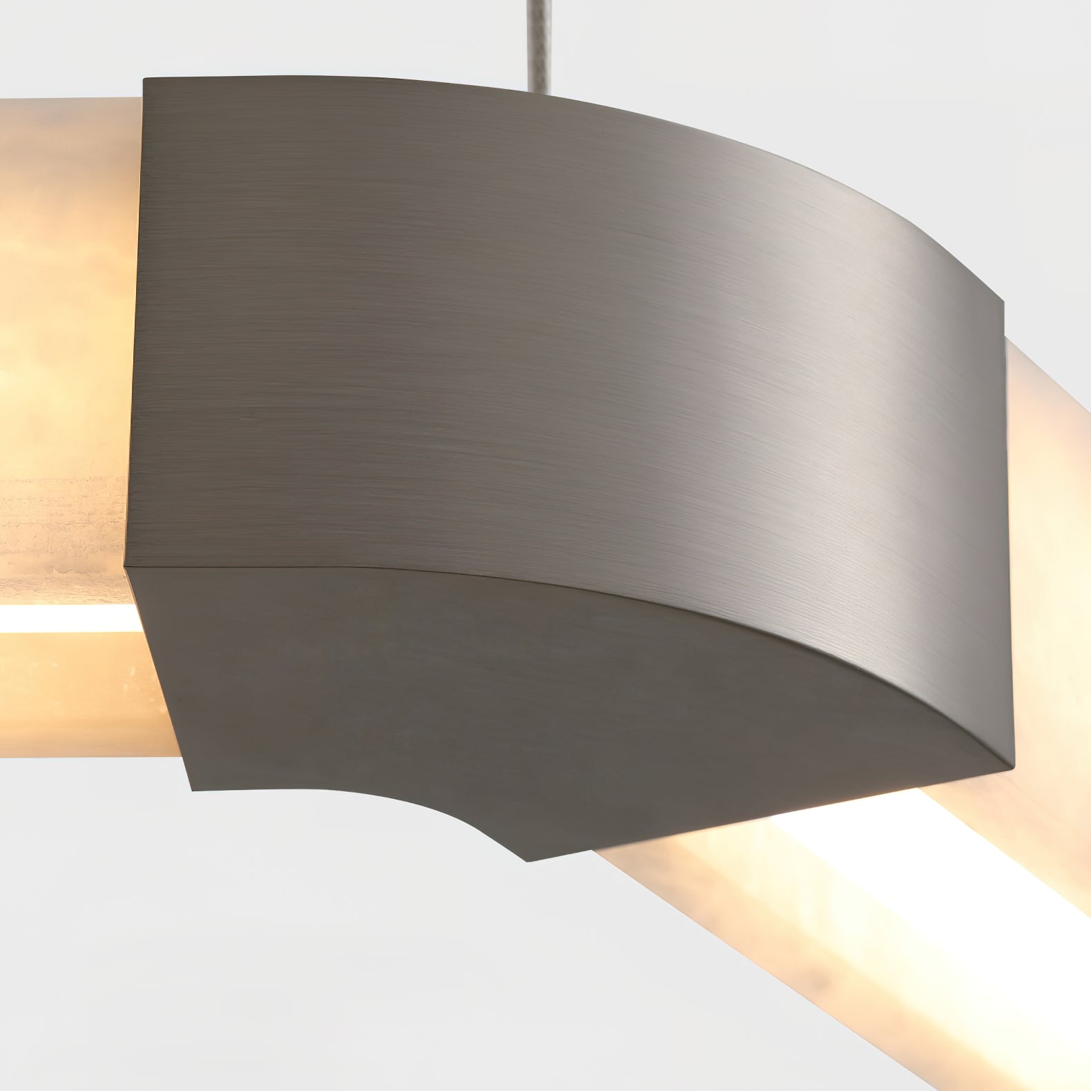 Detail of a brushed nickel corner cap on the Clérachic Hexagonal Alabaster Chandelier, joining two warmly lit stone bars.