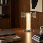 Lit Clérachic glass table lamp on a dark wooden desk, with a laptop, a stack of books and a stone tray beside it.