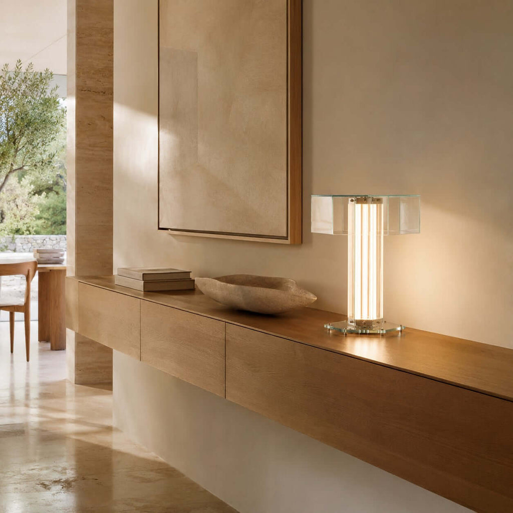 This Clérachic glass lamp glows on a wall-hung wooden shelf, next to a stone bowl and a small stack of books, in a bright hallway.