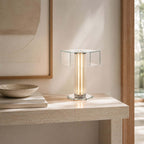 Close view of this Clérachic glass table lamp, its hexagonal top and glowing column on a stone console, with a bowl on books to the left.