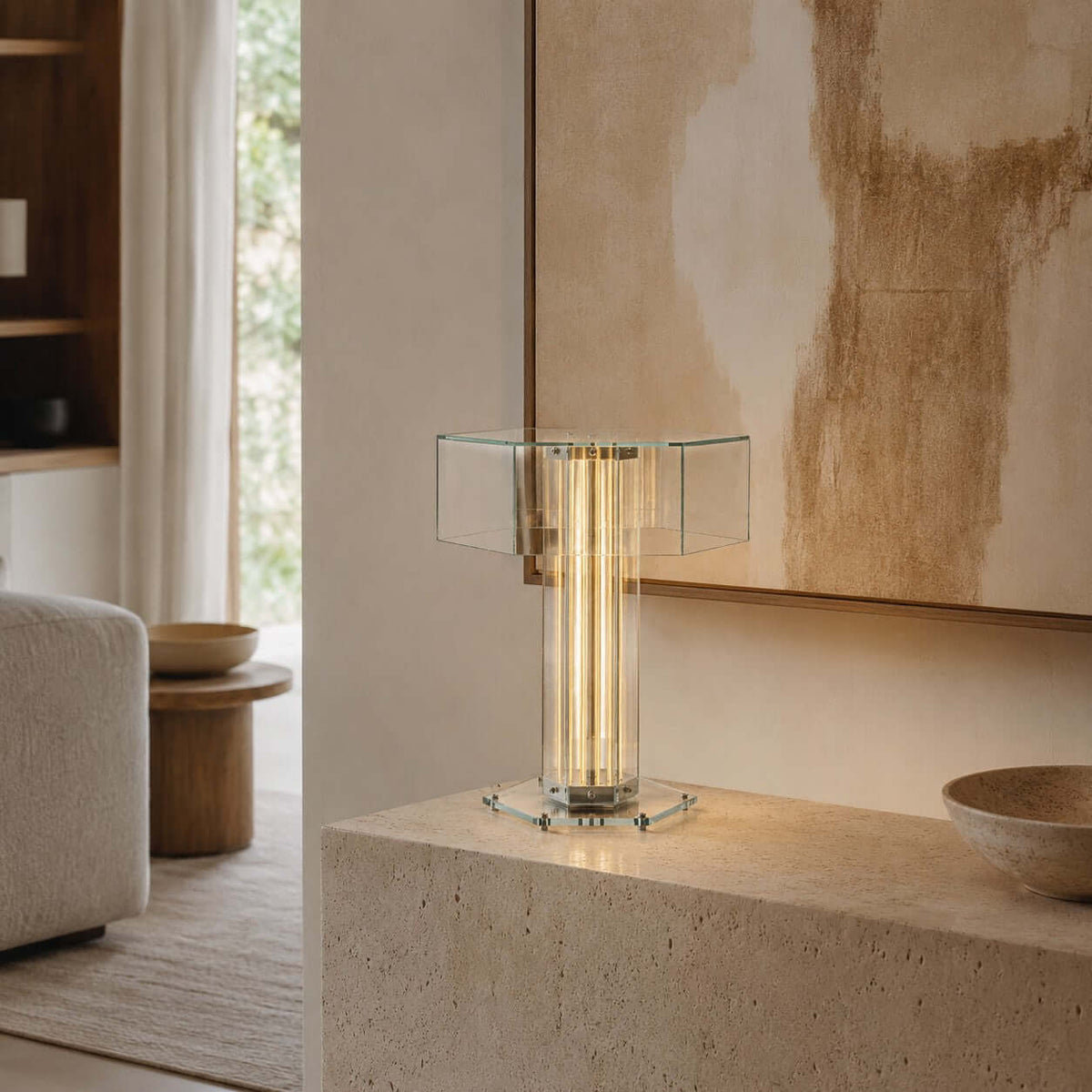 Clérachic table lamp with a lit centre column and a clear glass top on a stone block, in front of a large abstract painting.