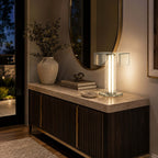 This Clérachic lamp lights up a stone-topped dark sideboard in an entrance, below a round mirror and beside a stone vase.