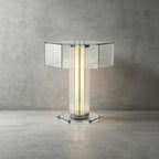 The clear hexagonal glass top, glowing column and glass base of this Clérachic table lamp, against a concrete-look wall.