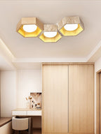 Three-cell Clérachic ceiling light over a wardrobe and dressing table, the hexagons lit warm gold in a pale bedroom.