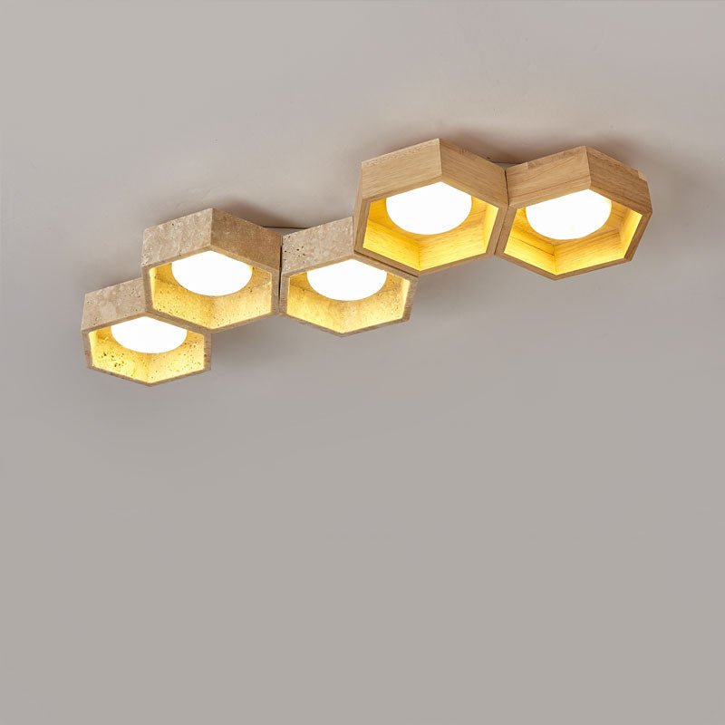 Five hexagons in a stepped diagonal, travertine and light wood, on this Clérachic ceiling light lit warm against grey.
