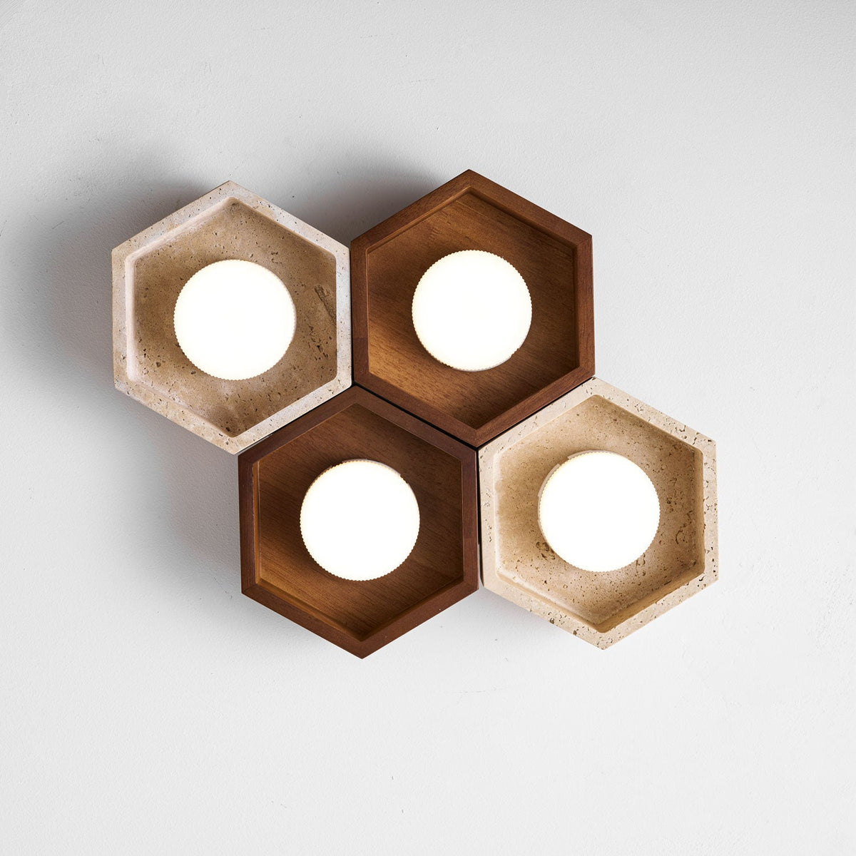 Four lit hexagons, two walnut and two travertine, of this Clérachic ceiling light shown from below on a pale backdrop.