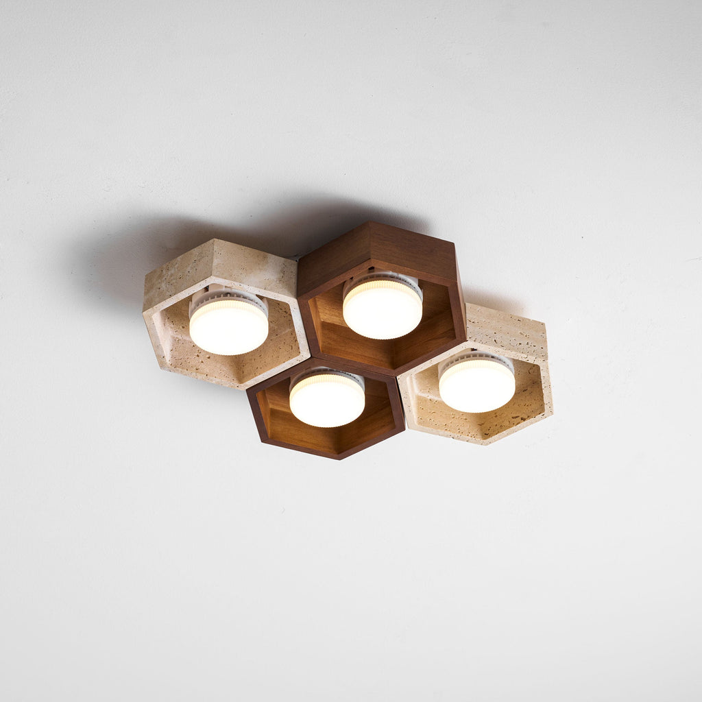 Four lit hexagons, walnut and travertine, of this Clérachic ceiling light seen at an angle against a white ceiling.