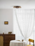 Small Clérachic ceiling light far above a round table with a lace cloth, a walnut sideboard and a yellow chair.
