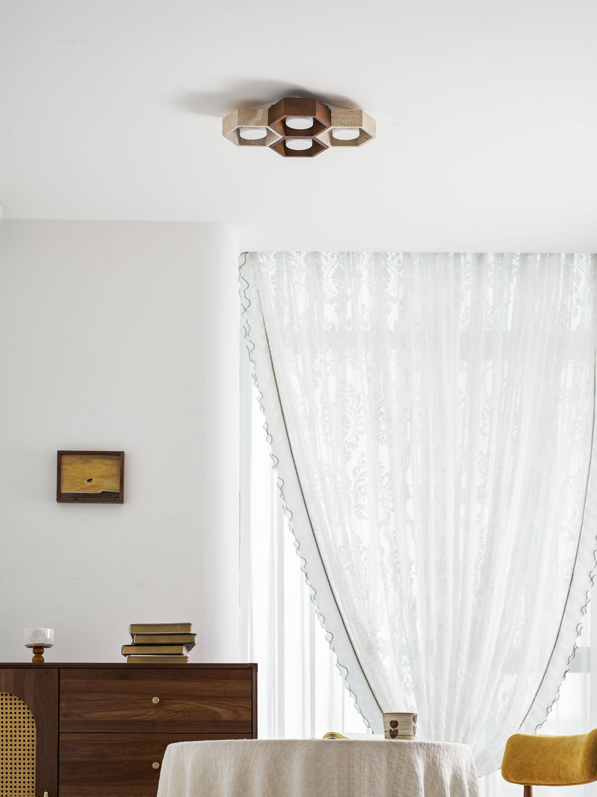 Four-cell Clérachic ceiling light seen far above a lace curtain, a walnut sideboard with a rattan door and a small framed picture.