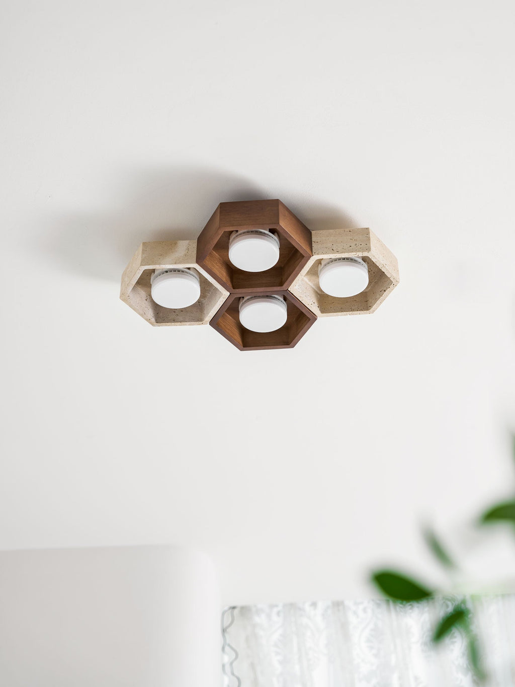Four-cell Clérachic ceiling light, unlit, with a walnut-toned centre, on a white ceiling near the edge of a green plant.