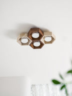 Four-cell Clérachic ceiling light, unlit, with a walnut-toned centre, on a white ceiling near the edge of a green plant.