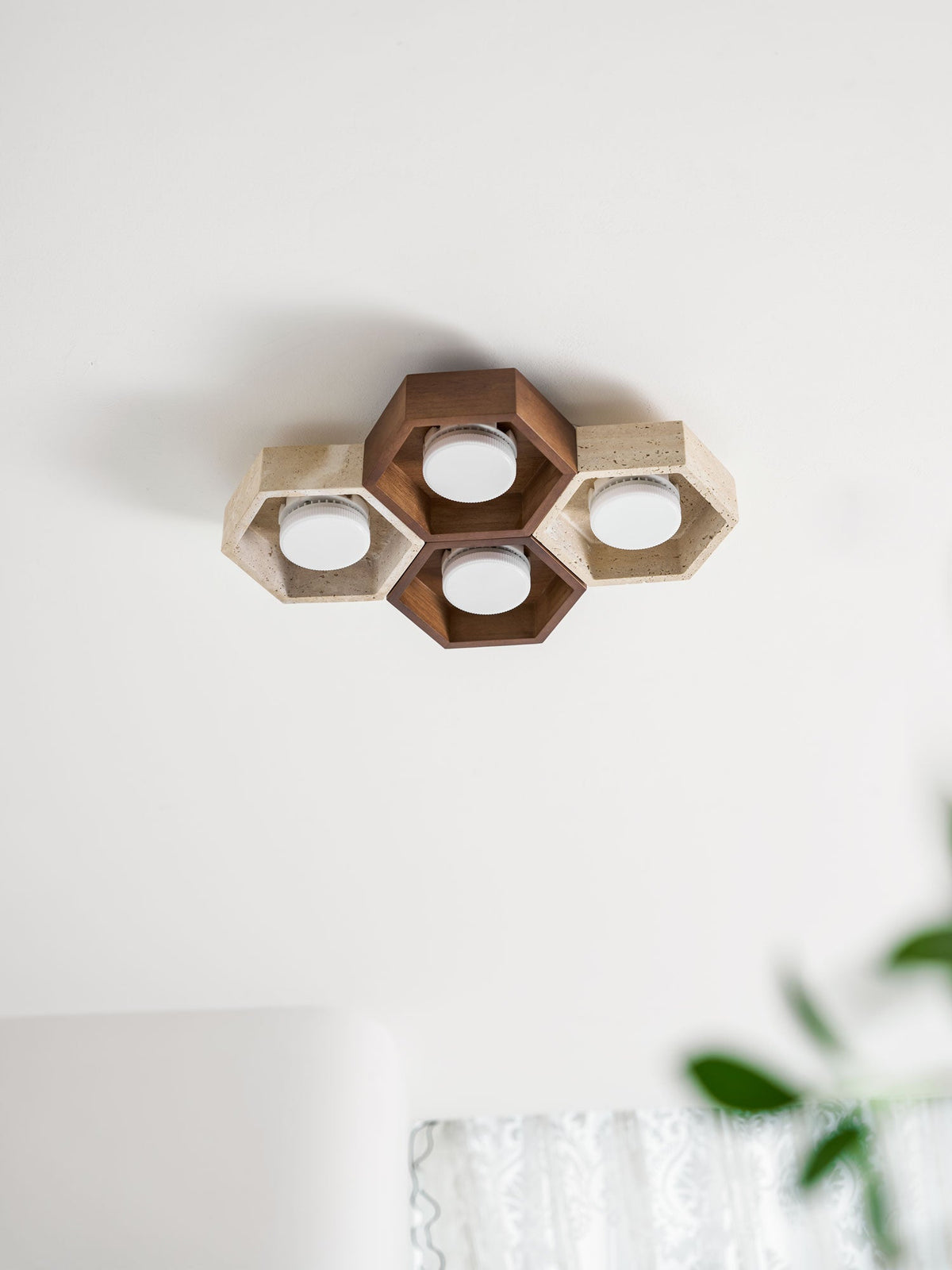 Four-cell Clérachic ceiling light, unlit, with a walnut-toned centre, on a white ceiling near the edge of a green plant.
