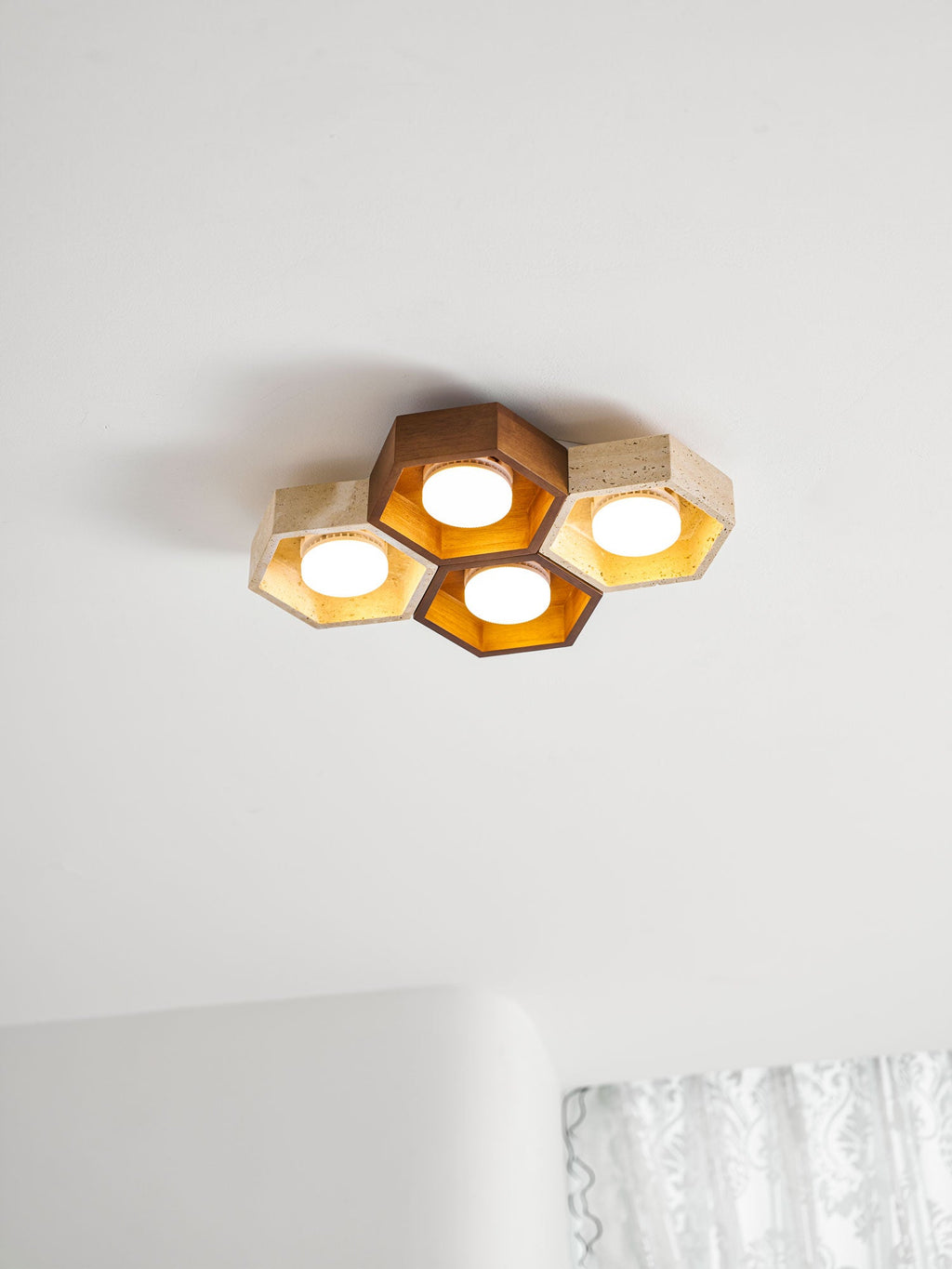 Lit four-cell Clérachic ceiling light on a white ceiling, its walnut and travertine hexagons glowing warm gold.