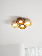 Lit four-cell Clérachic ceiling light on a white ceiling, its walnut and travertine hexagons glowing warm gold.