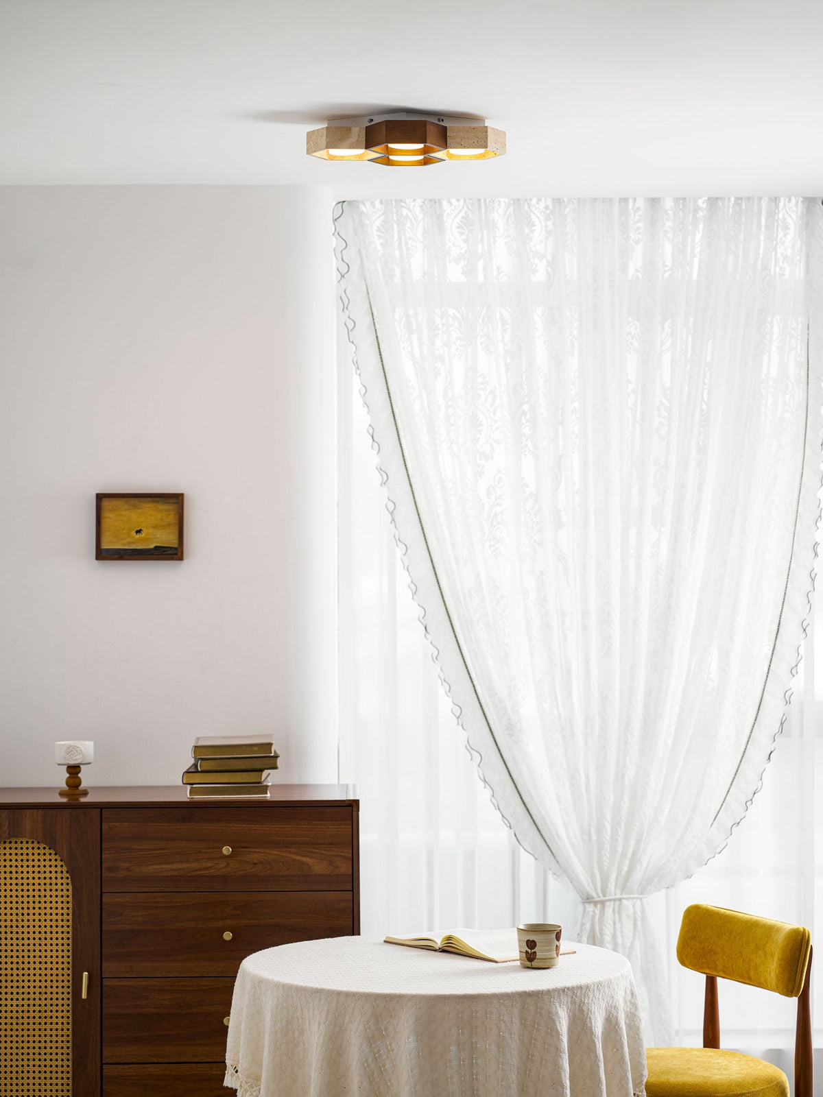 Low-profile Clérachic ceiling light lit above a dining corner with a round table, a lace curtain and a yellow chair.