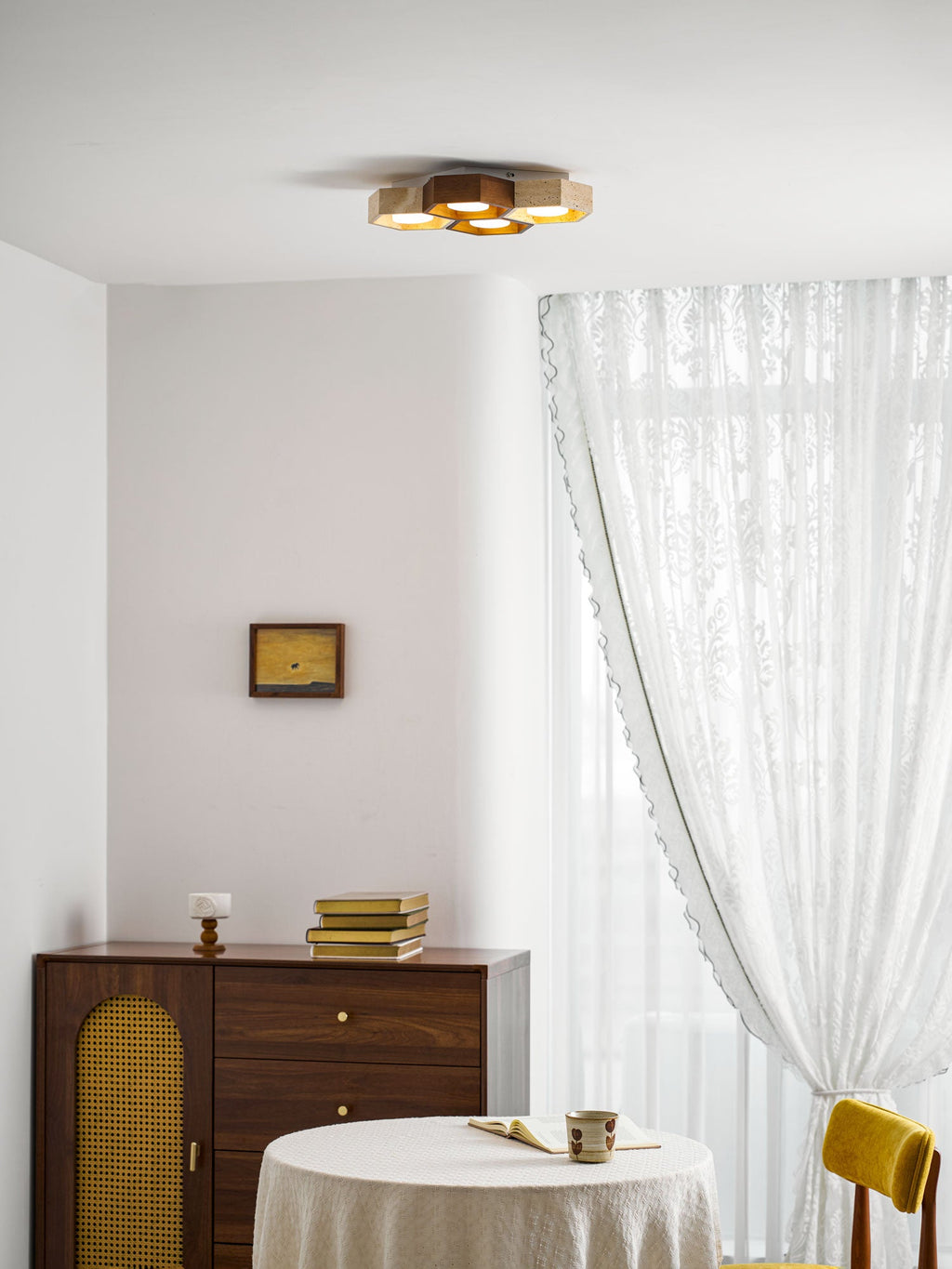 Clérachic ceiling light glowing high on a white ceiling over a walnut sideboard, a lace-clothed table and a yellow chair.