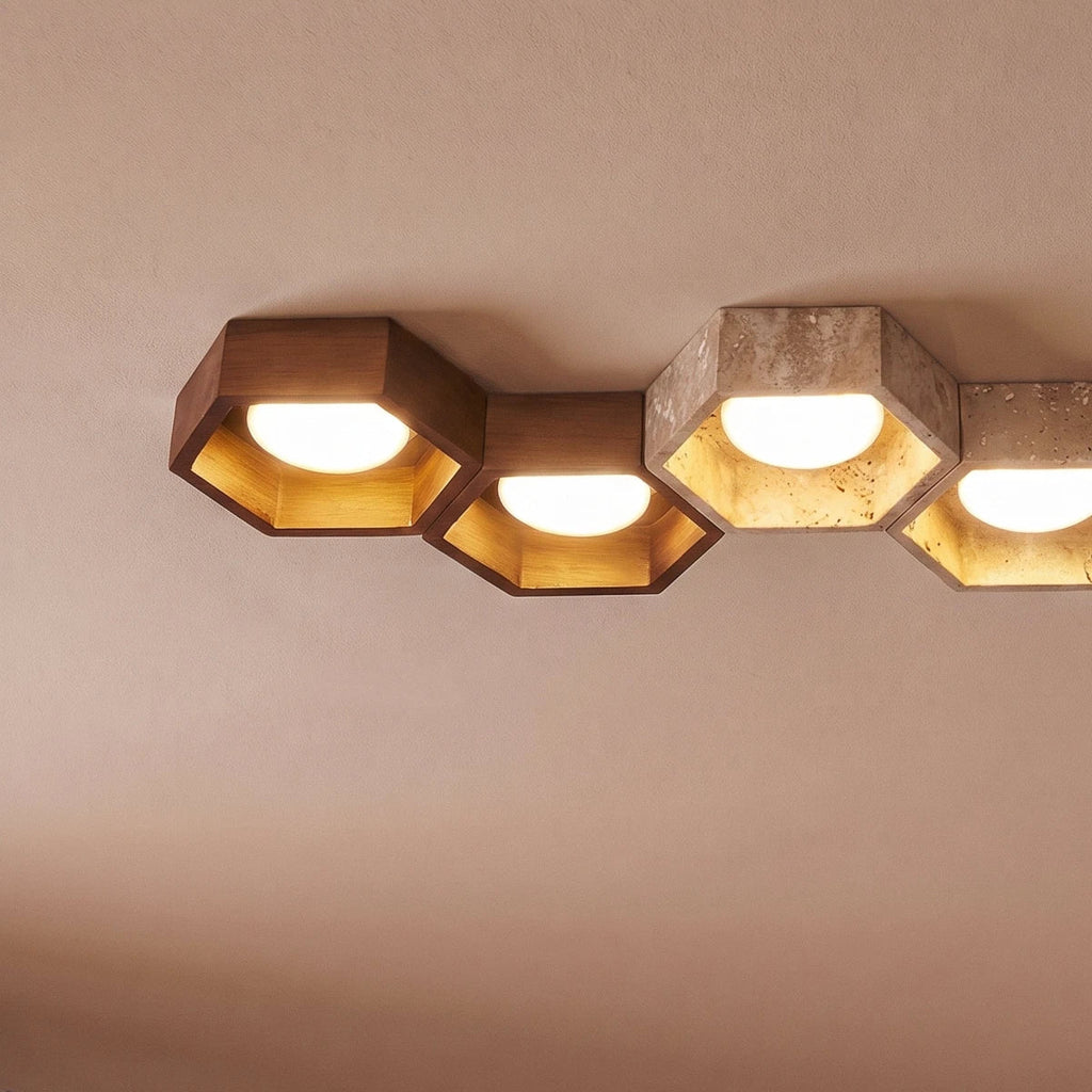 Close-up of Clérachic hexagonal ceiling lights in walnut and travertine, gold-leaf interiors glowing around white opal globes.
