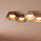 Close-up of Clérachic hexagonal ceiling lights in walnut and travertine, gold-leaf interiors glowing around white opal globes.