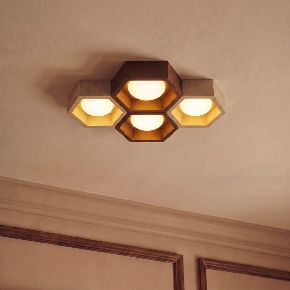 Clérachic four-head ceiling light seen from below, walnut and travertine hexagons with gold-leaf linings beside cornice mouldings.