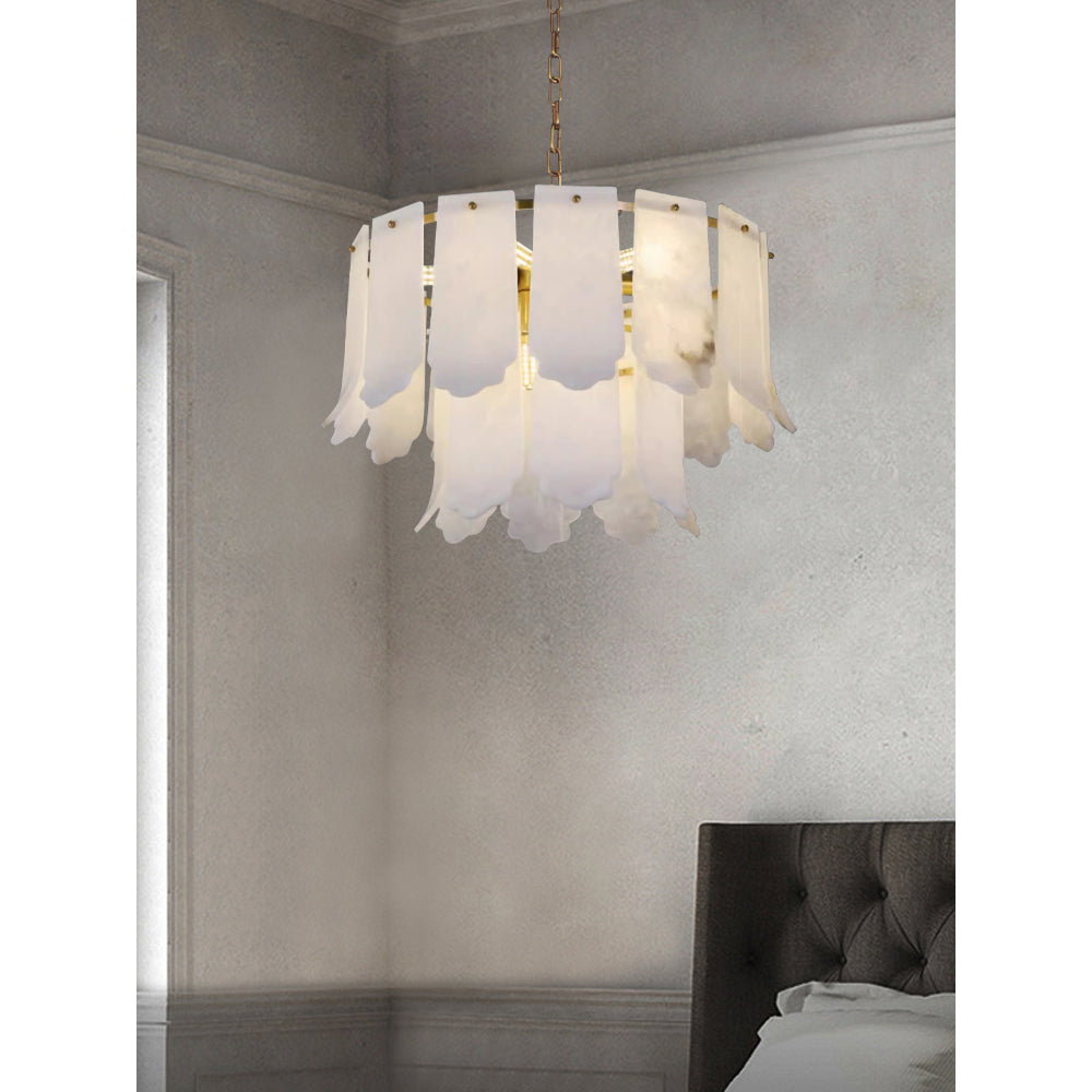 The Clérachic Hue Alabaster Chandelier lit in a pale plaster bedroom corner, hanging beside a dark tufted headboard.
