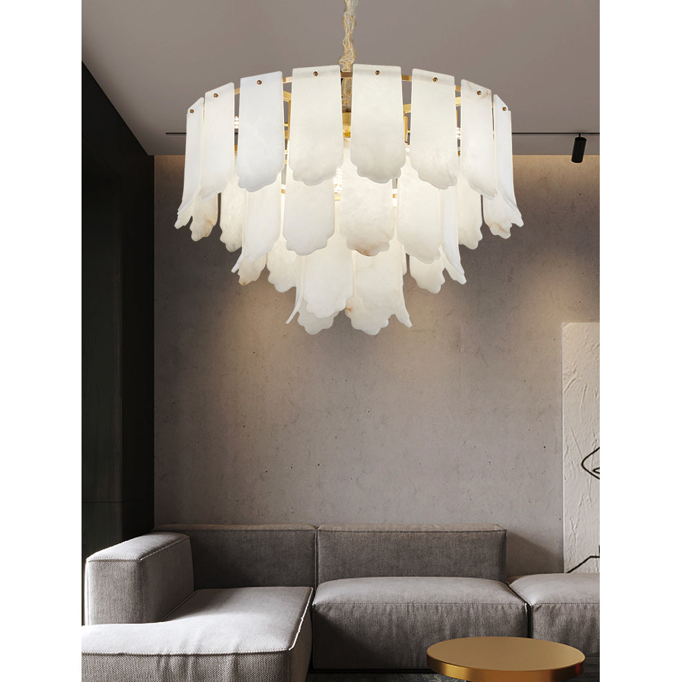 The Clérachic Hue Alabaster Chandelier glowing above a grey sectional sofa against a raw concrete wall in a living room.