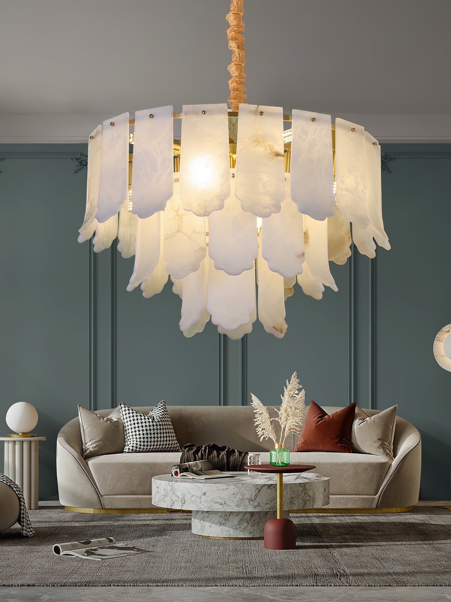 Close view of the Clérachic Hue Alabaster Chandelier lighting a curved sofa and marble coffee table against a deep teal panelled wall.