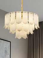 Low angle on the Clérachic Hue Alabaster Chandelier, the brass ring and all three tiers of stone visible beside a heavy curtain.