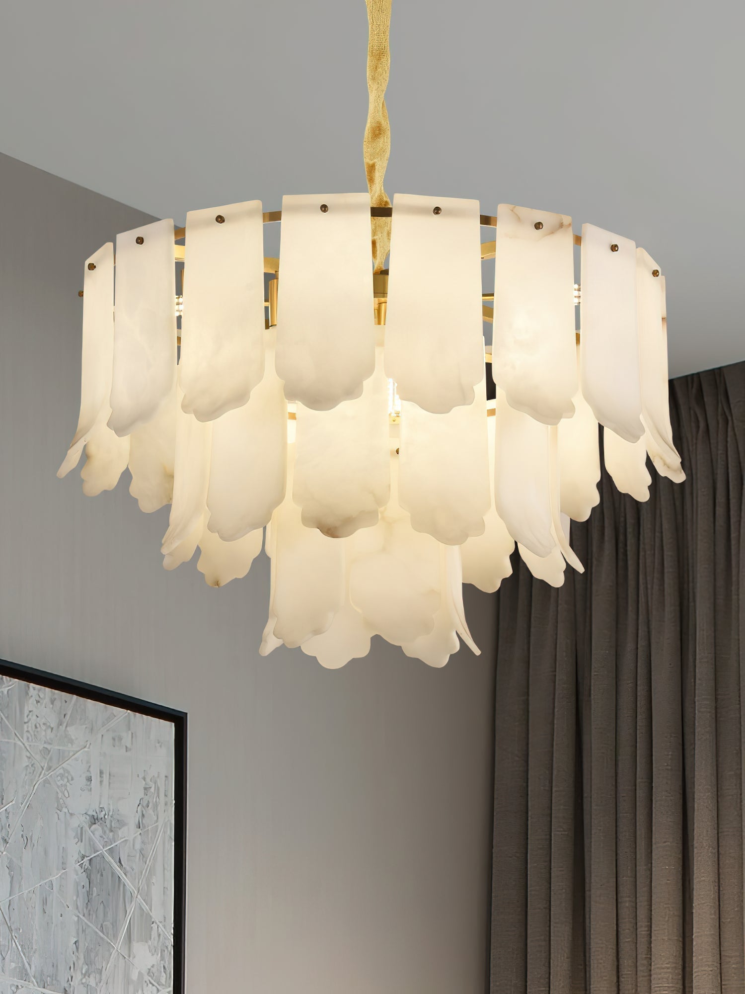 Low angle on the Clérachic Hue Alabaster Chandelier, the brass ring and all three tiers of stone visible beside a heavy curtain.
