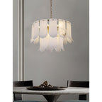 The nine-light Clérachic Hue Alabaster Chandelier on a brass chain above a dining table dressed with a dark stone bowl.